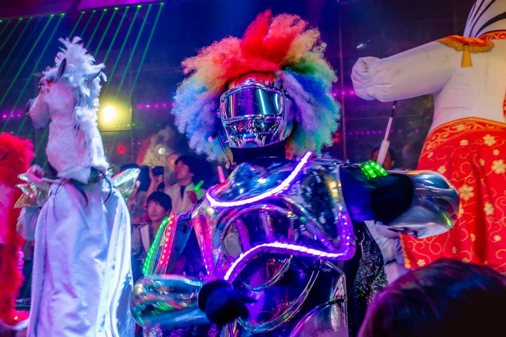 A man in a neon robot costume with a rainbow colored afro.